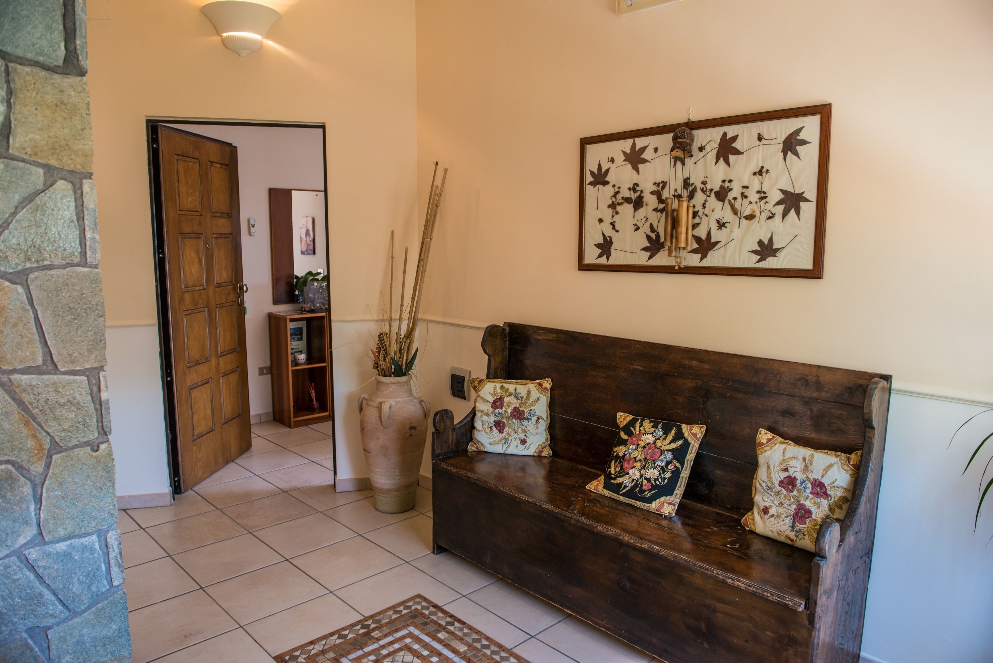 Un banc en bois agrémenté de coussins à motifs floraux, un mur en pierre et une œuvre d’art botanique encadrée accrochée au mur.