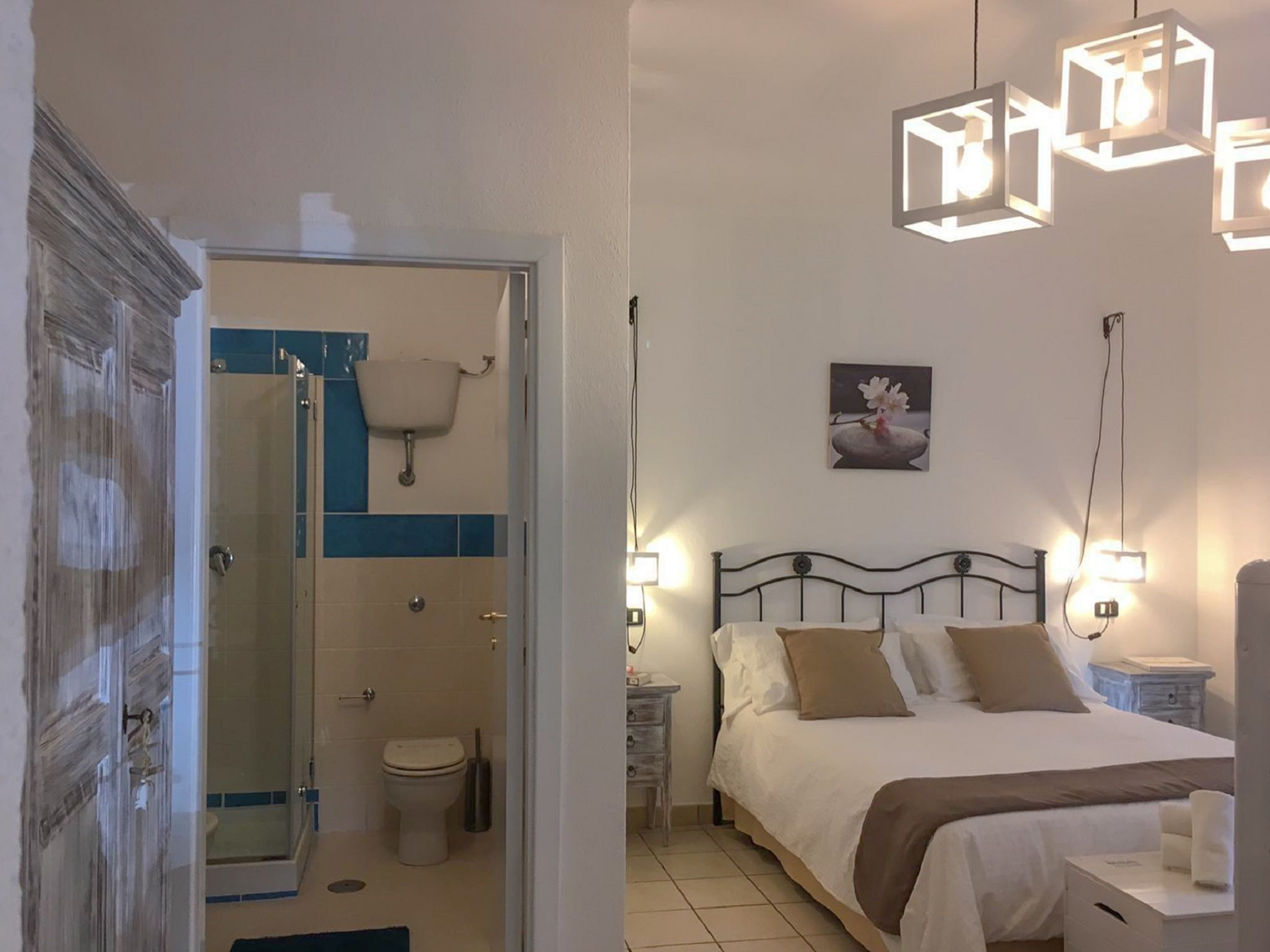 Un dormitorio con cama, mesitas de noche, lámpara de pared, y un baño con ducha, inodoro y lavamanos.