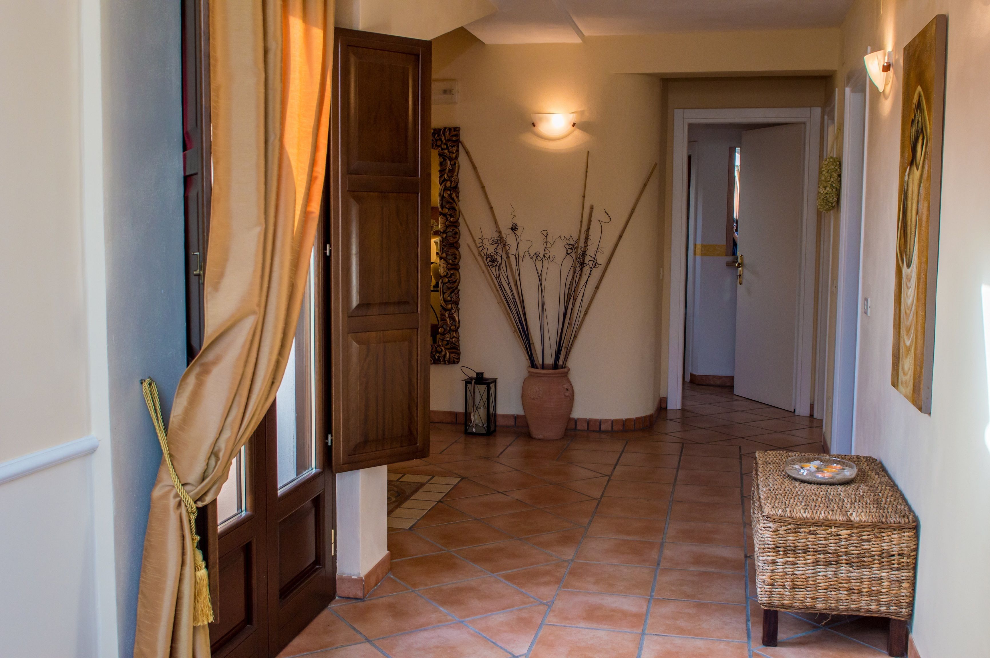 A hallway with a wooden door, a vase with branches, a lantern, and a wicker bench.