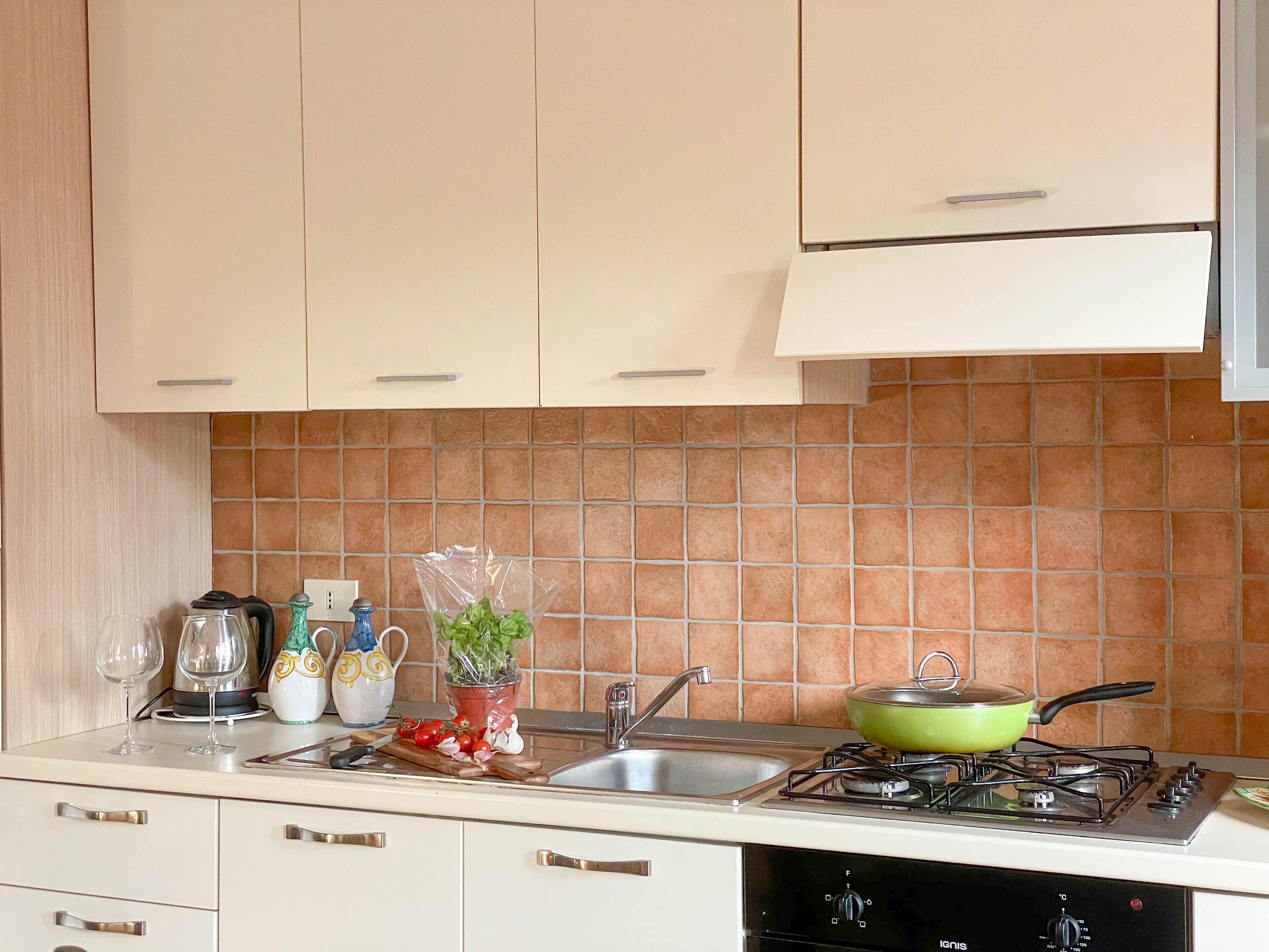 Una cocina con armarios de colores claros, salpicadero de azulejos, estufa a gas y varios utensilios de cocina sobre la encimera.