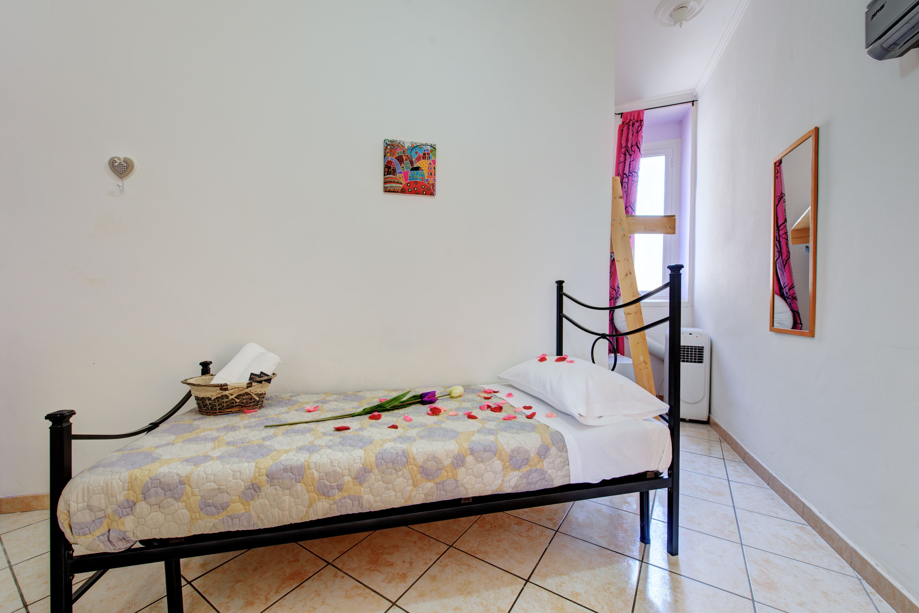 Un lit simple avec une couette, une table de chevet avec un panier, et un climatiseur fixé au mur.