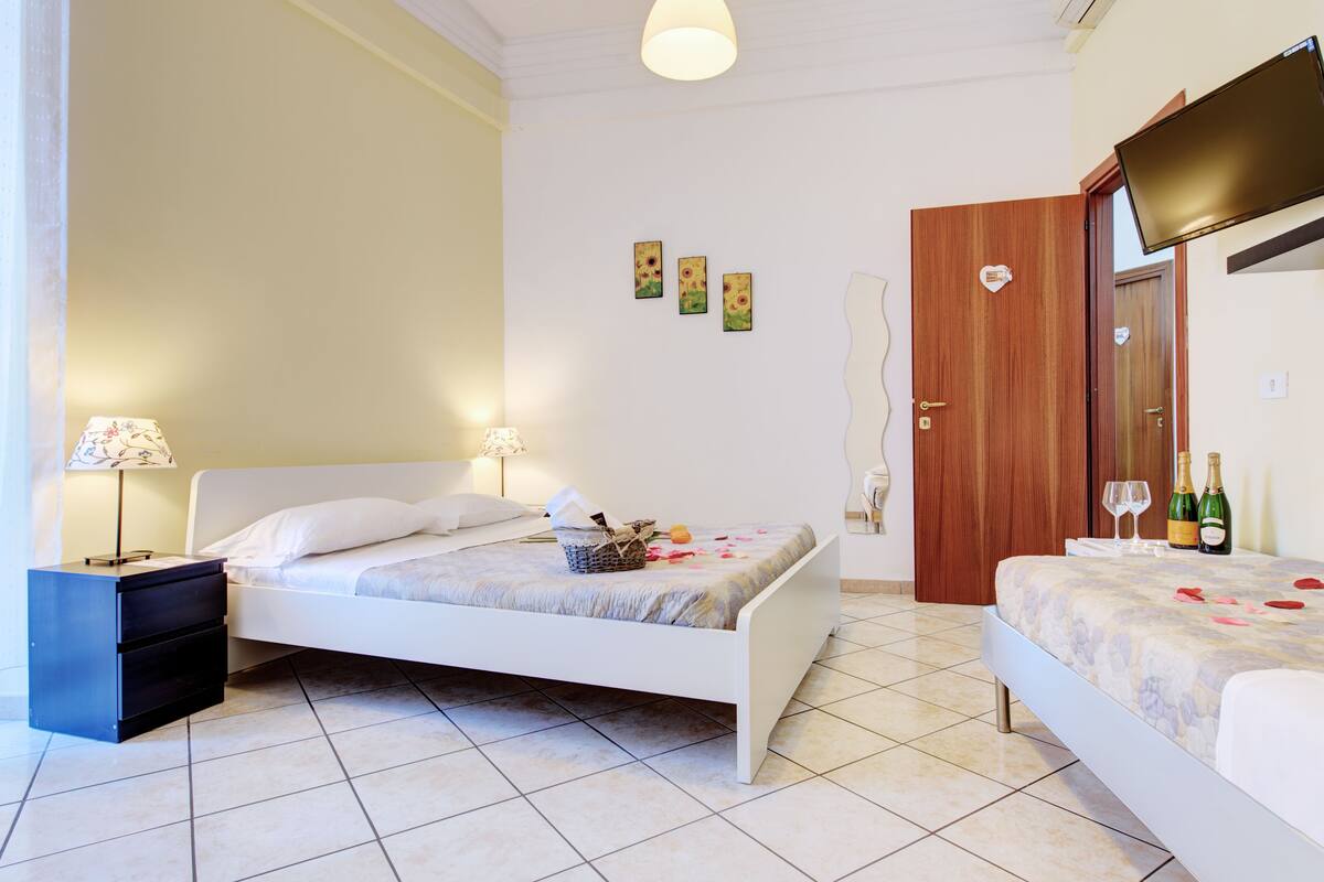 Une chambre avec deux lits, une table de chevet, une lampe et une porte dotée d’un miroir.
