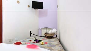 Ein Schlafzimmer mit einem Bett, einem an der Wand montierten Fernseher, einem Heizkörper und einem Korb mit Handtüchern.