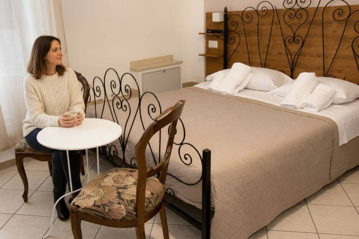 Une chambre d’hôtel avec un lit, une chaise, une petite table et une fenêtre avec des rideaux.
