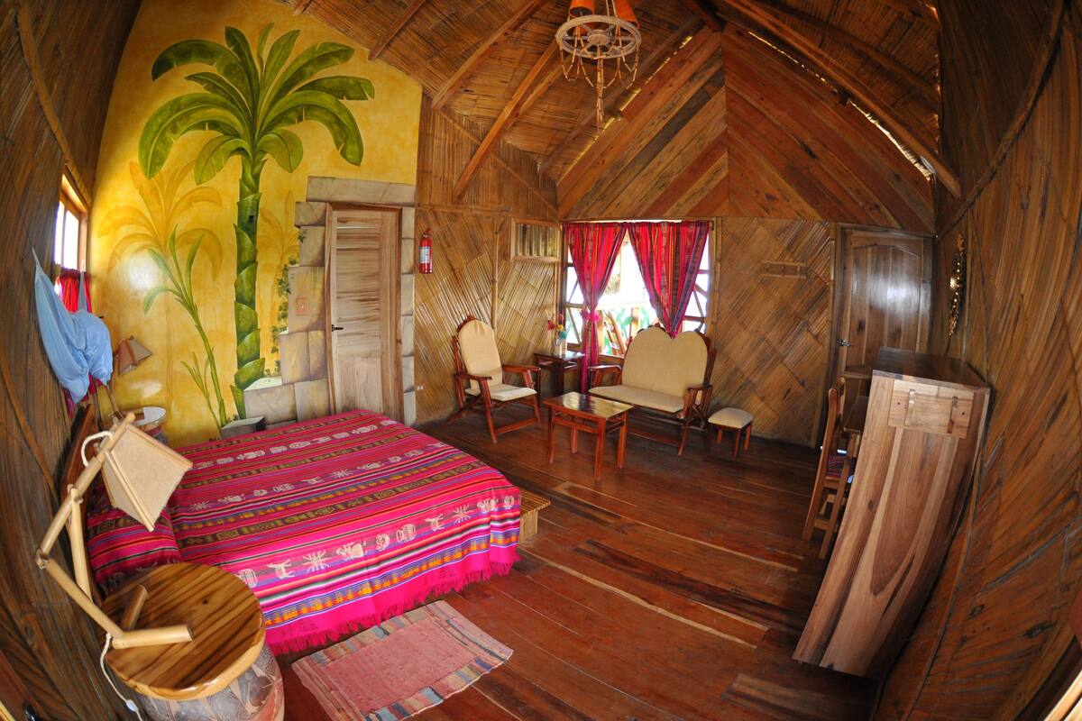 A rustic wooden room with a bed, chairs, a table, and a large wooden door.