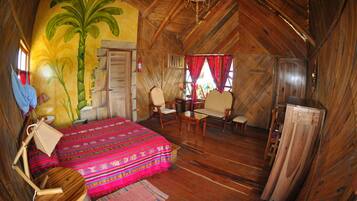 A rustic wooden room with a bed, chairs, a table, and a large wooden door.