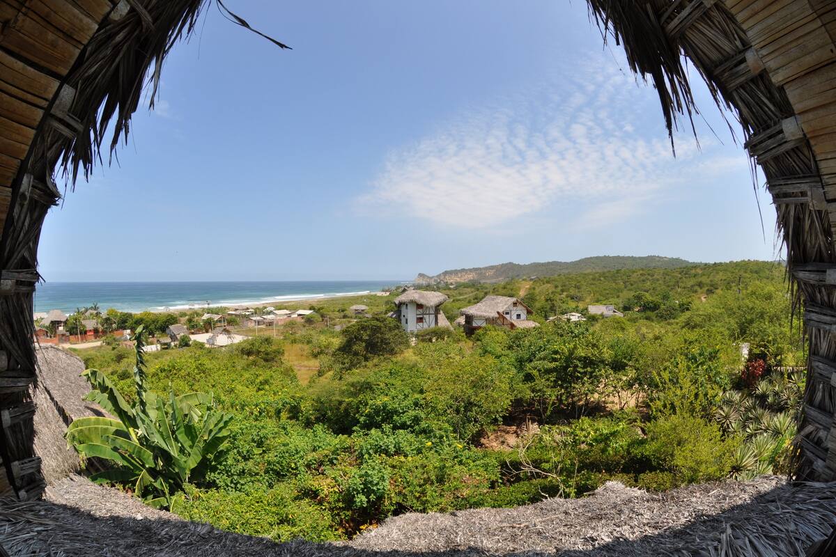 A view from a thatched-roof structure overlooking a coastal area with houses and greenery.