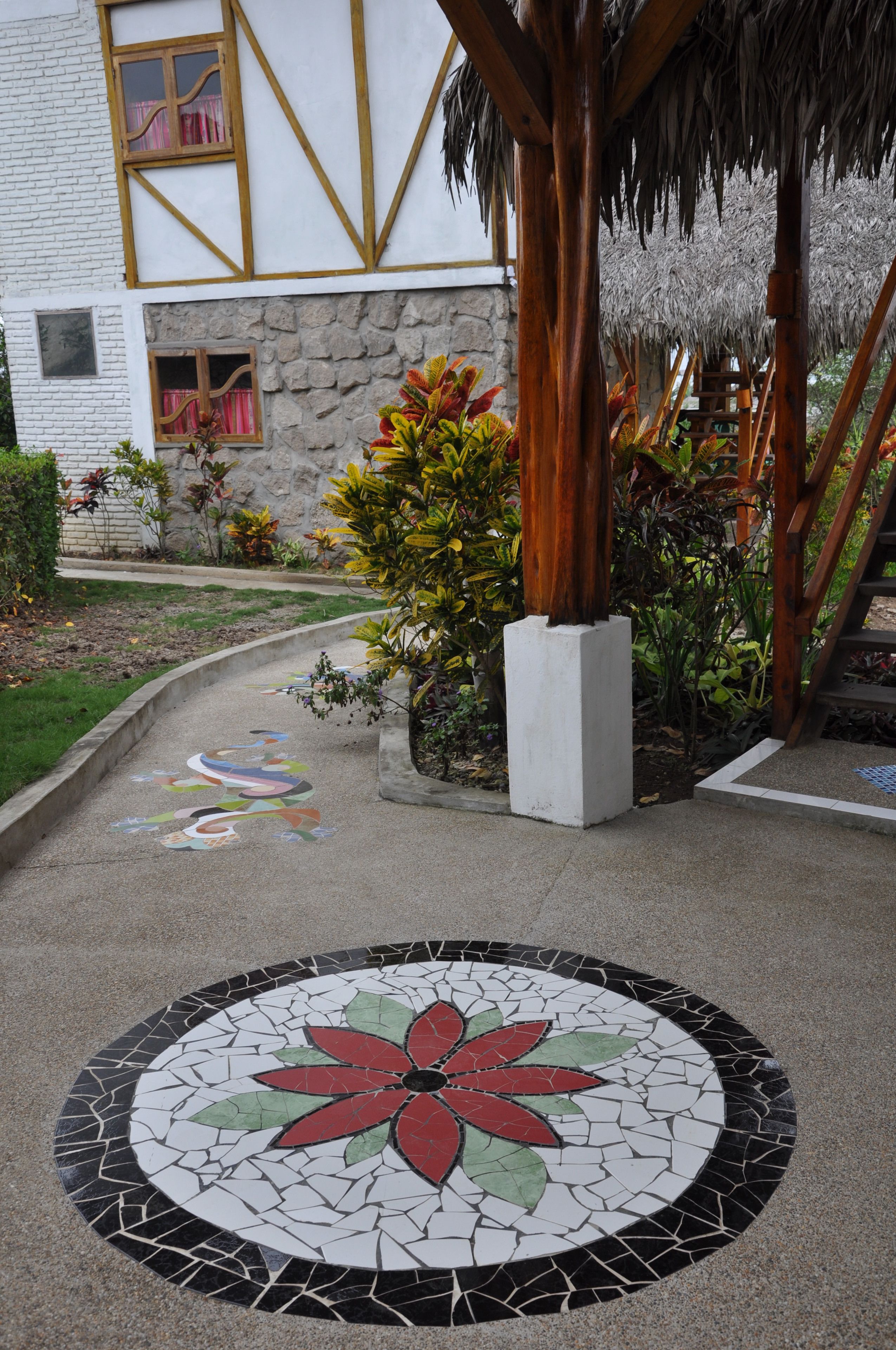 A courtyard with a mosaic floor design, a stone wall, and a wooden pergola.