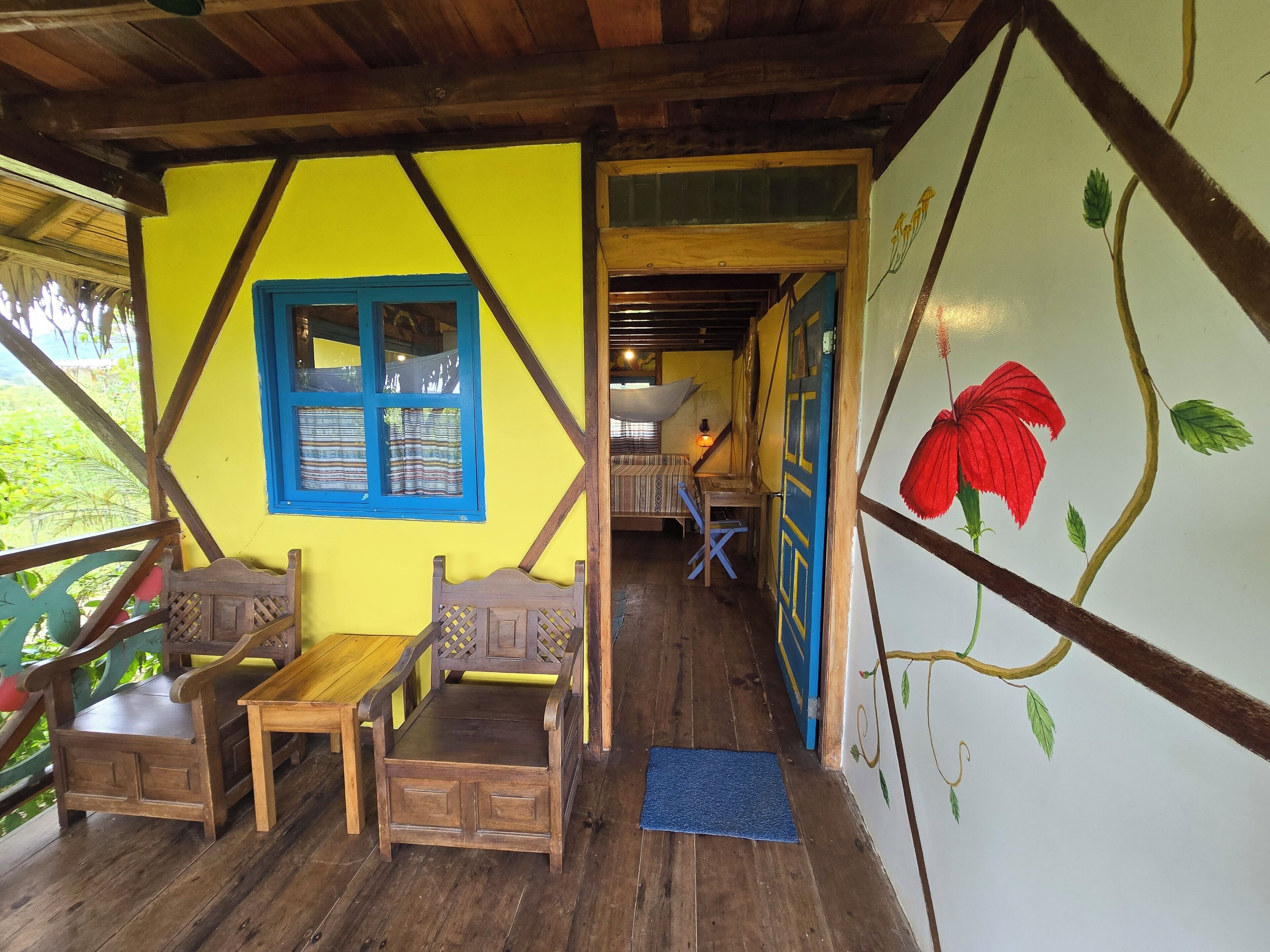 Un intérieur en bois avec un banc, une table et une fresque représentant une fleur rouge sur le mur.
