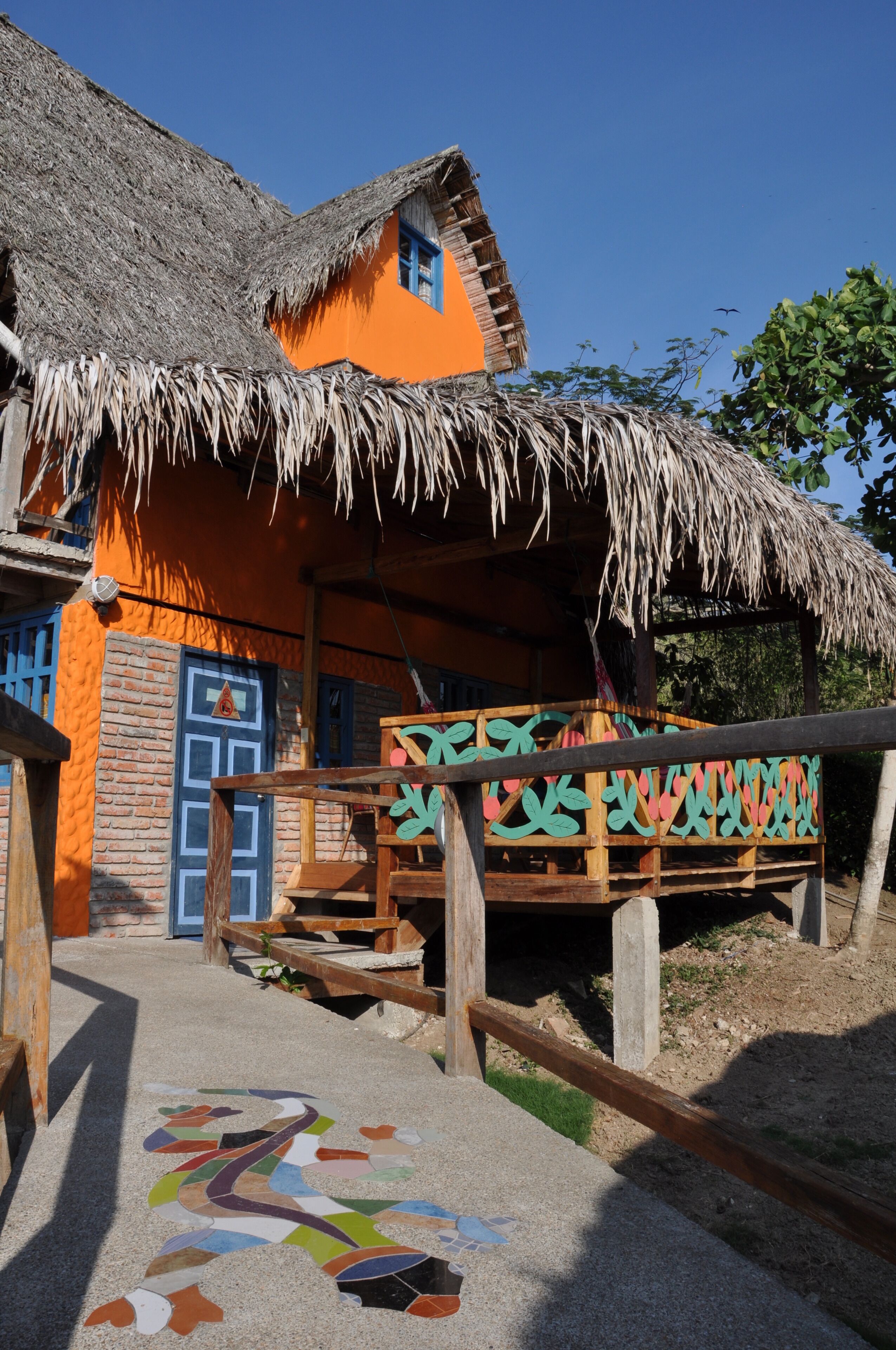A traditional building with a thatched roof, a colorful exterior, and a wooden staircase leading to a porch.