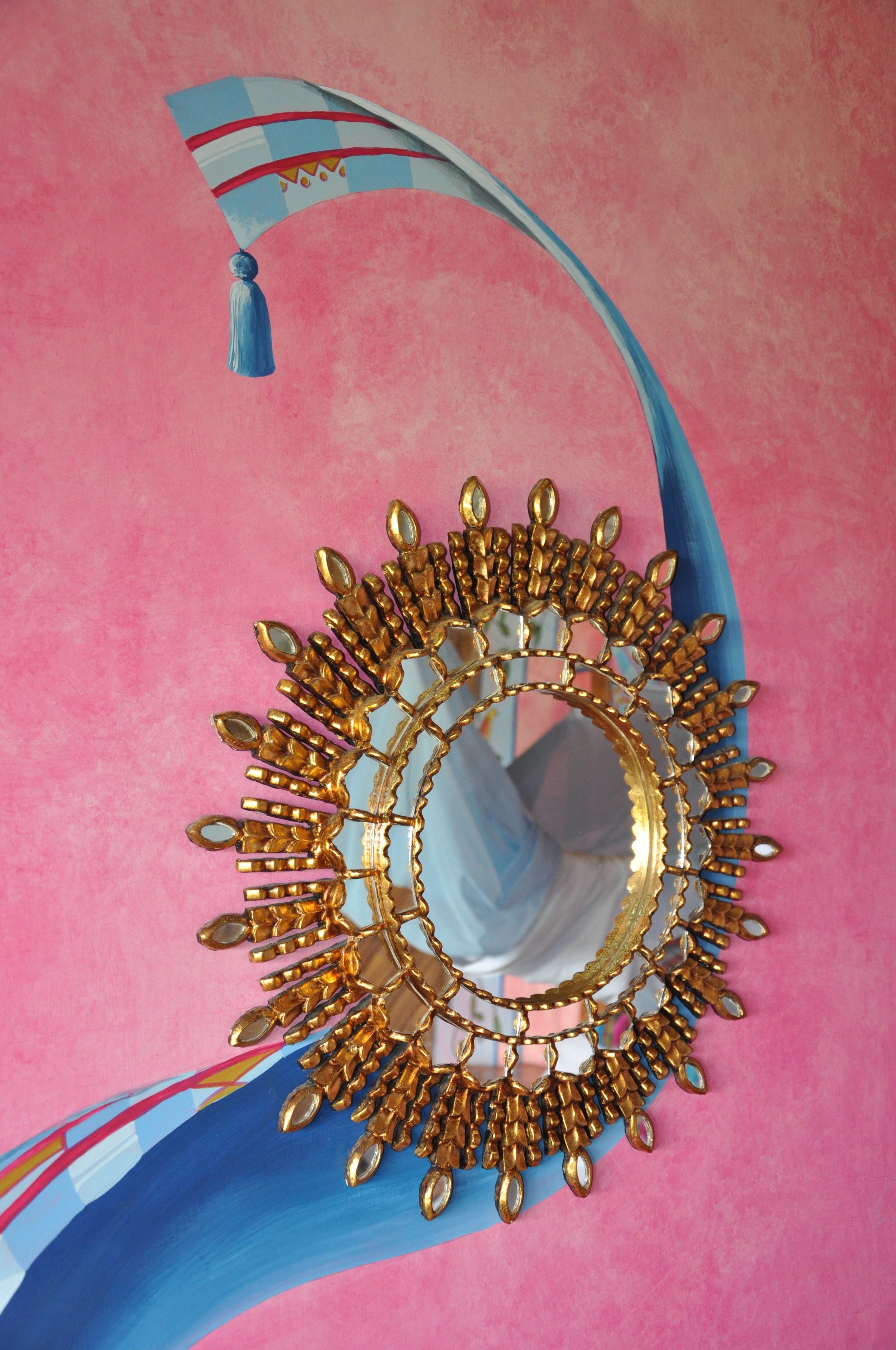 A decorative mirror with a gold frame and tassel hanging from its top.