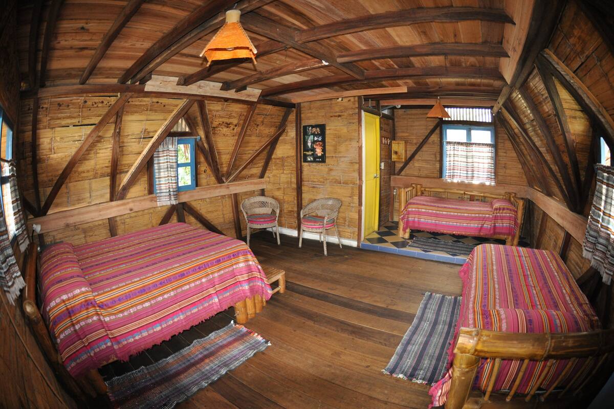 A rustic wooden room with two beds, wicker chairs, and a small table.