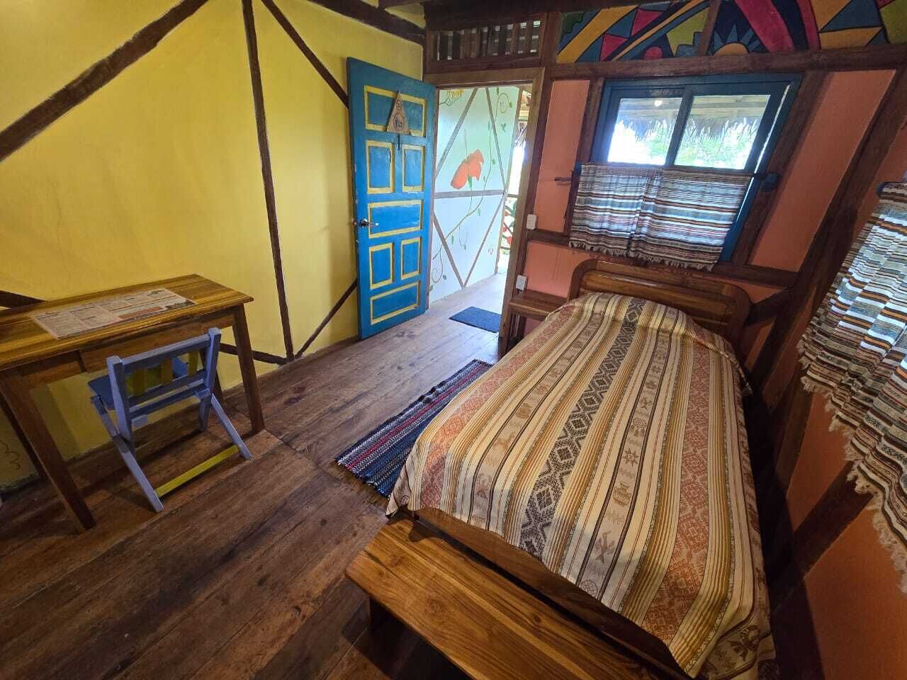 Een kamer met een houten bed, een klein tafeltje en een kleurrijke deur.