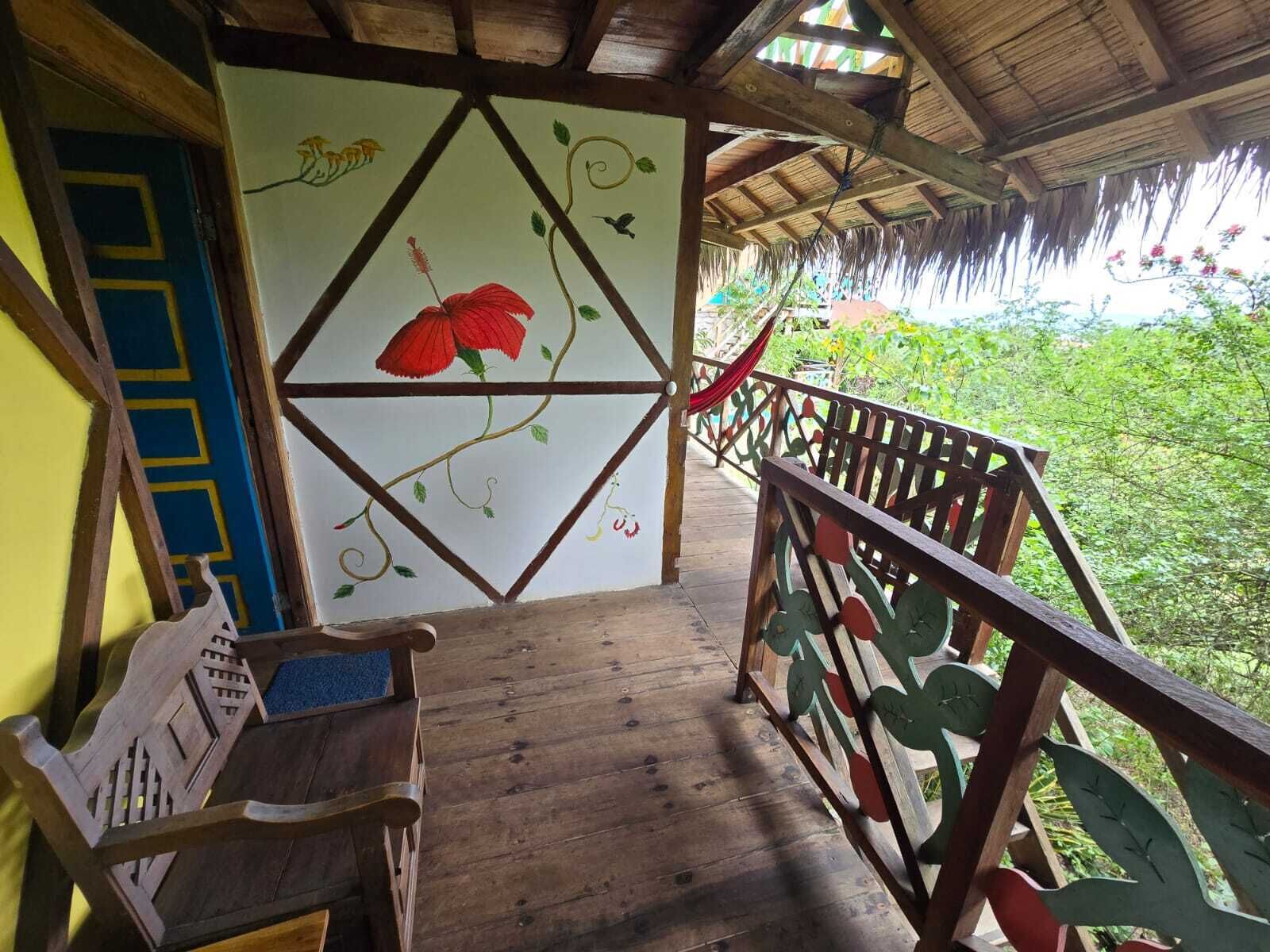 A wooden balcony with a decorative railing, a bench, and a wall with a floral mural.