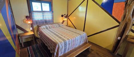 Een kamer met een bed, een raam met gordijnen, een muur met geometrische patronen en een houten plafond.