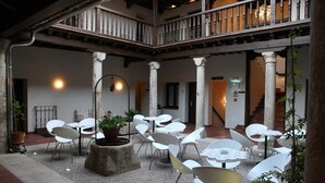 A spacious outdoor patio with white chairs and tables, stone columns, and a wooden balcony railing. - Evenia Alcalá Boutique Hotel (Alcala de Henares)