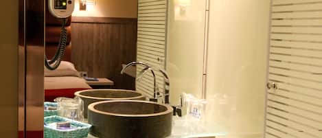 A modern bathroom with a large mirror, a sink with a glass countertop, and two white towels on the counter.