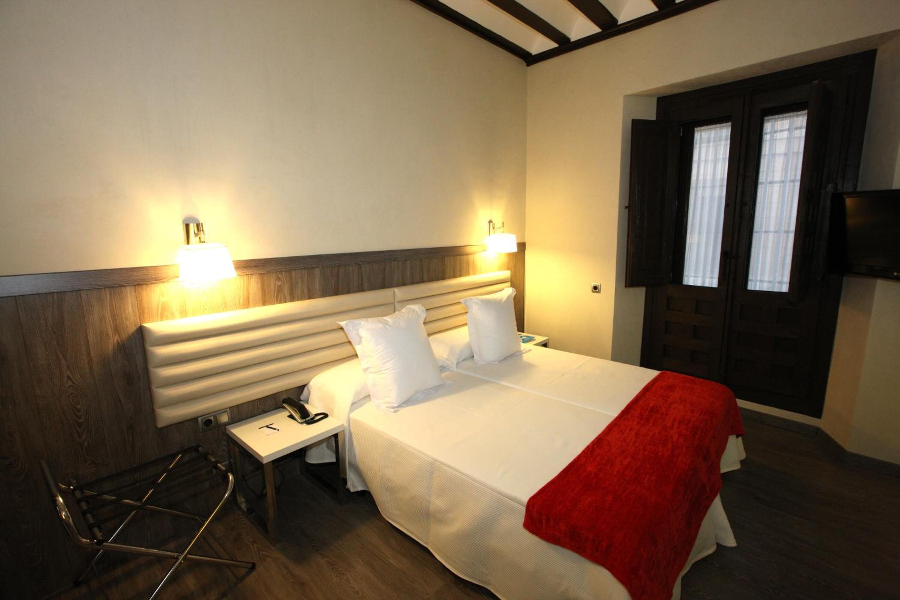Una habitación de hotel con cama, lámparas de noche, televisión y ventana.