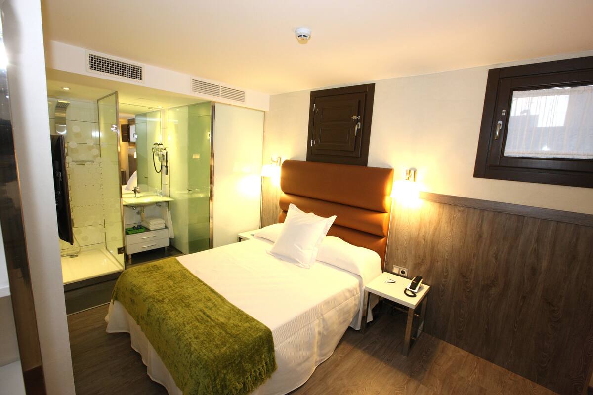A hotel room with a bed, bedside table, and a mirror.