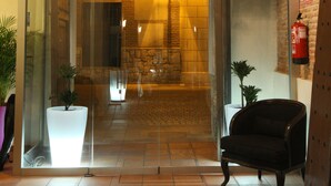 A hotel lobby with a modern chandelier, a black armchair, and a glass door marked "SALIDA". - Evenia Alcalá Boutique Hotel (Alcala de Henares)