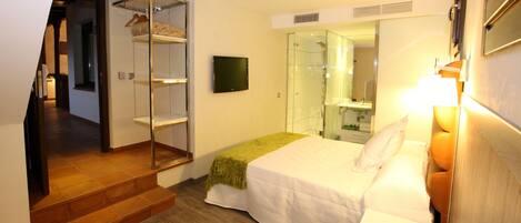 A hotel room with a bed, a bedside table, a mirror, a TV, and a closet with hanging clothes.