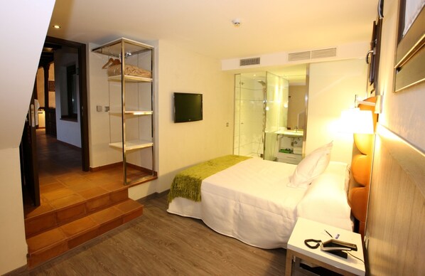 A hotel room with a bed, a bedside table, a mirror, a TV, and a closet with hanging clothes.
