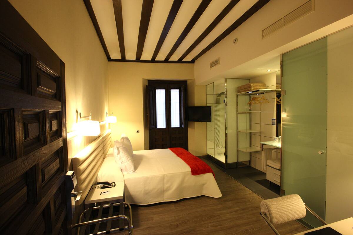 A hotel room with a bed, bedside table, lamp, and a walk-in closet with shelves and a mirror.