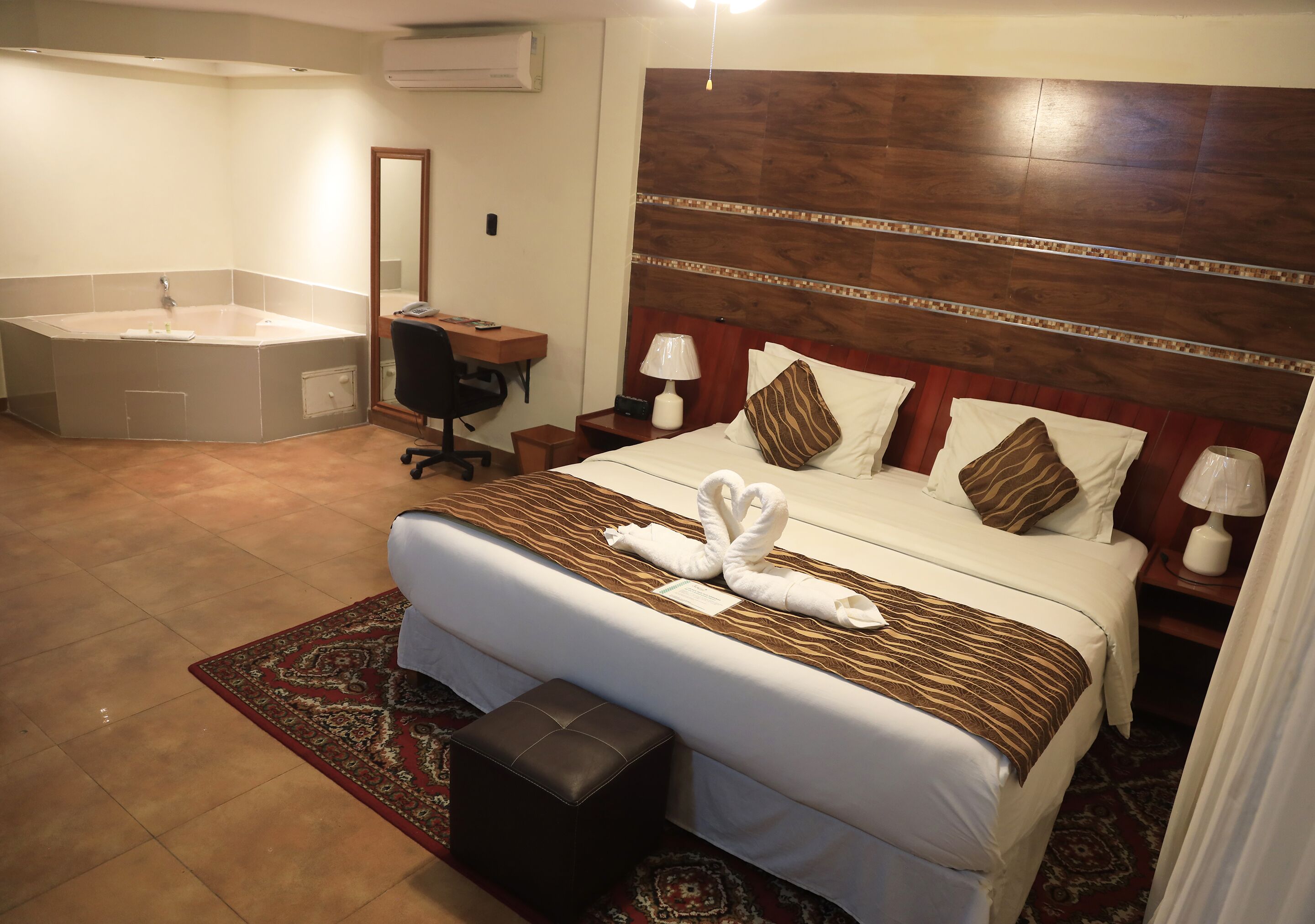 A hotel room with a large bed, a desk, a chair, a bathroom with a bathtub, and a mirror.