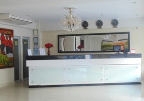 A hotel reception area with a large mirror, a chandelier, clocks, and a painting on the wall.