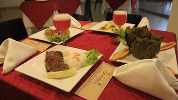 A dining table with red tablecloths, plates of food, and drinks.