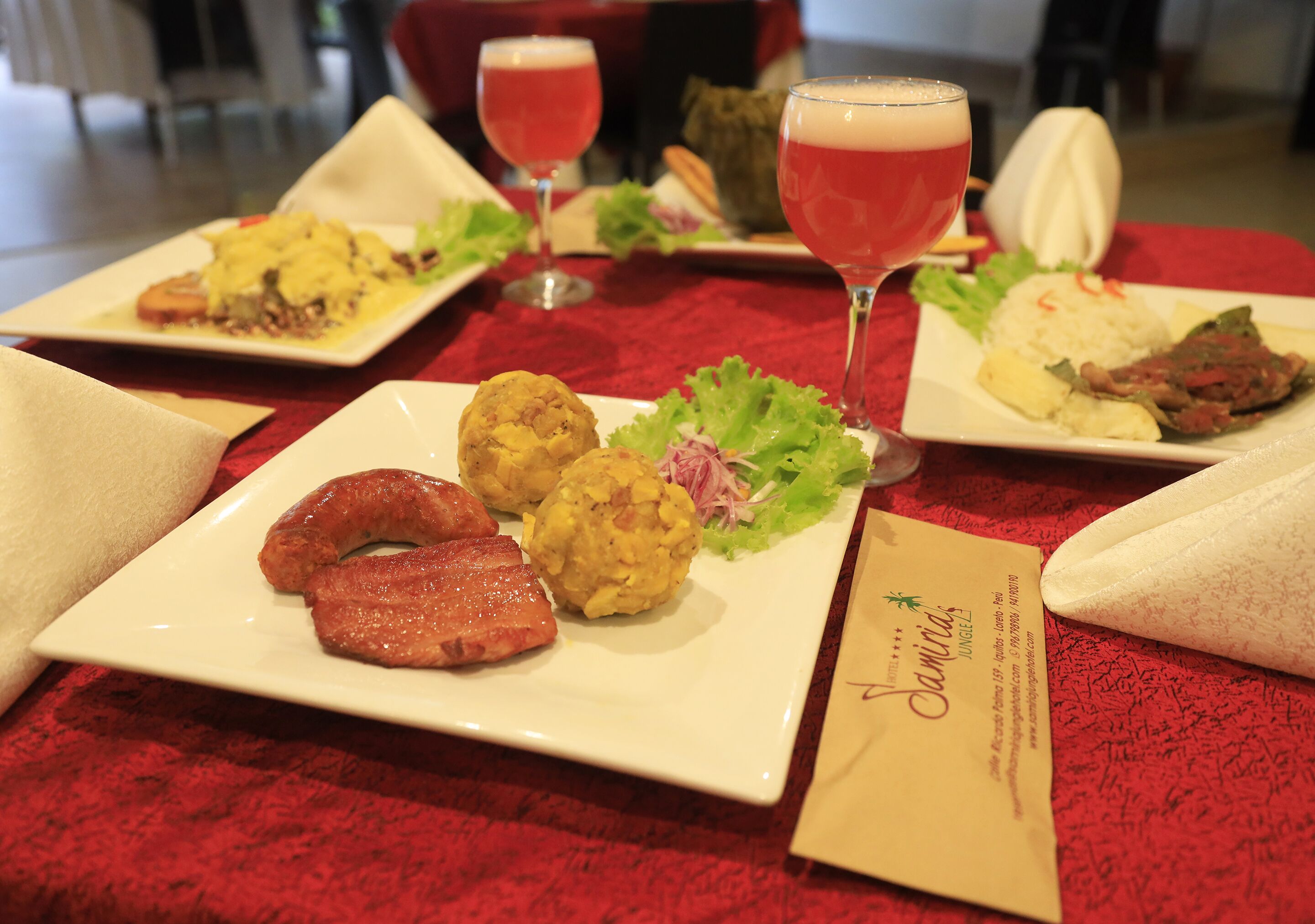 Una mesa servida con varios platos, incluyendo salchichas, albóndigas y arroz, junto con dos vasos de bebida roja.