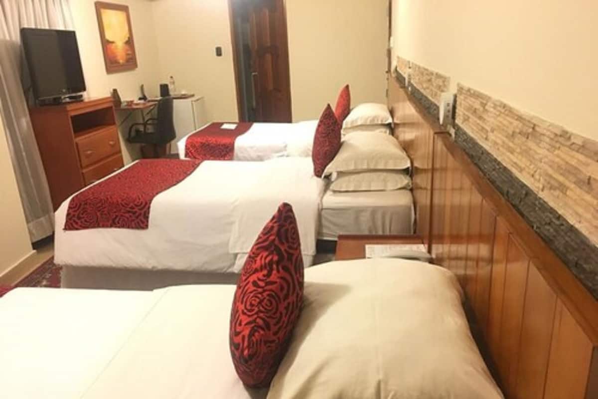 A hotel room with two beds, each with a red and white pillow, a wooden headboard, a desk with a chair, a television, and a painting on the wall.