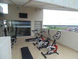 Un balcón con equipo de ejercicio, una puerta de cristal y vistas de la ciudad.
