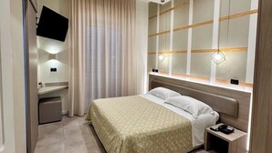 Una camera d'albergo moderna con un letto, un comodino, una TV e un grande specchio.