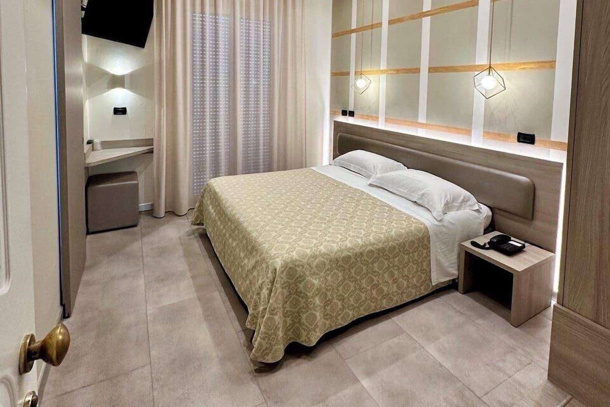 A modern hotel room with a bed, bedside table, TV, and a large mirror.