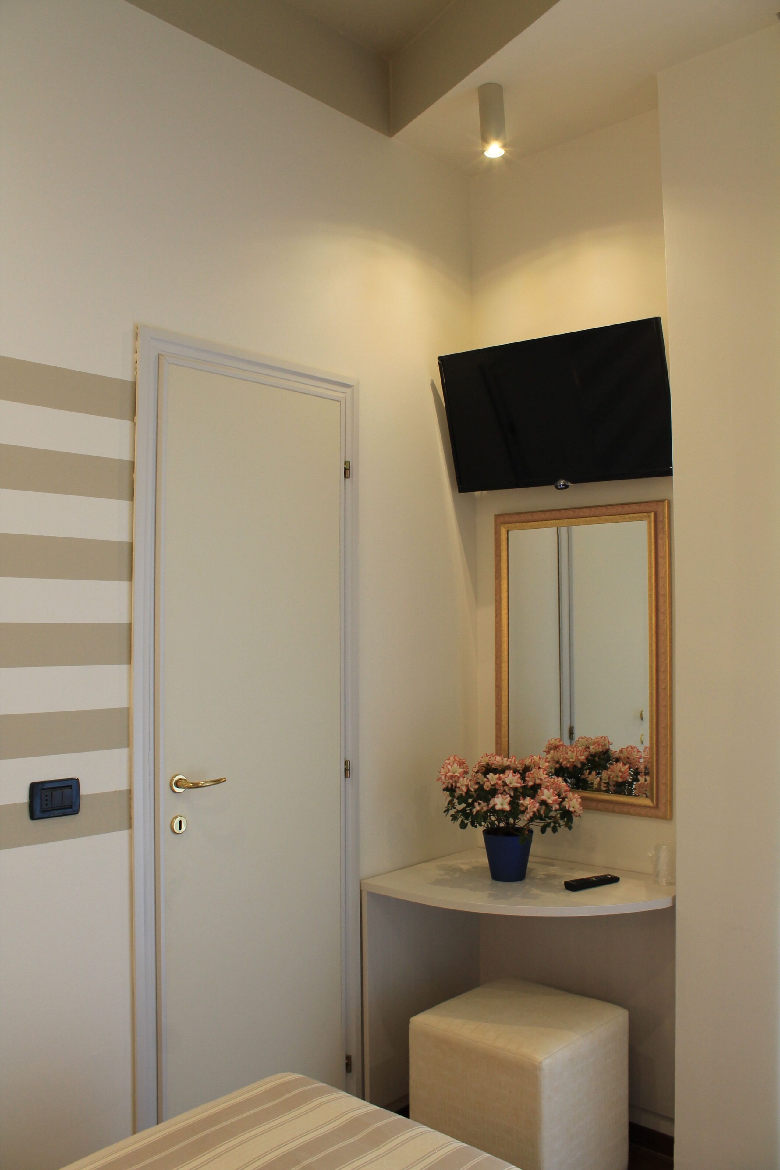 A room with a door, a small stool, a television mounted on the wall, and a potted plant on a counter.