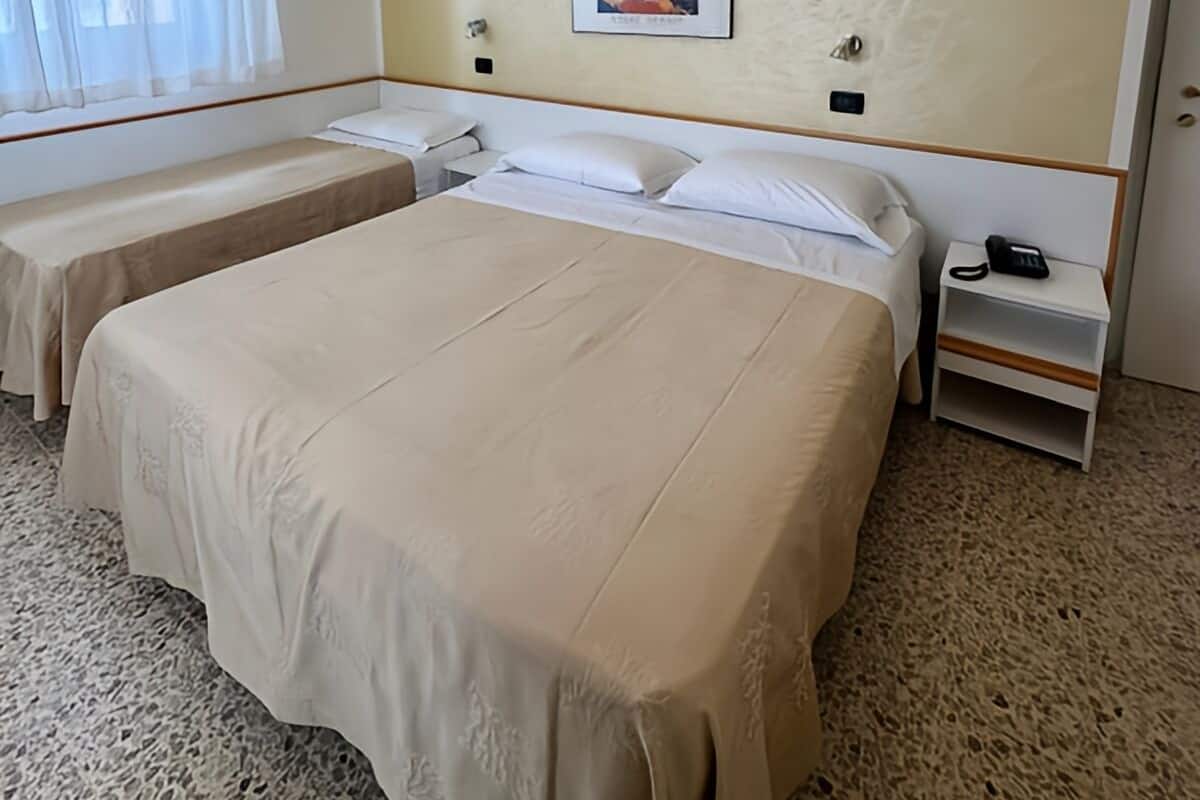 A hotel room with two beds, a large window with curtains, a wall-mounted picture, and a bedside table with a phone.