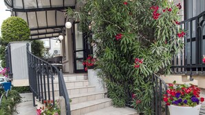Una scala conduce all'ingresso di un edificio, dotata di ringhiera in metallo nero e circondata da vasi con fiori rossi.