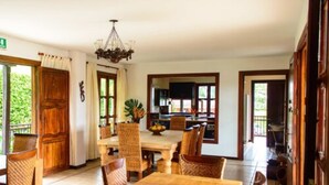 Un comedor con una mesa y sillas de madera, una araña y vistas a la cocina y al exterior.