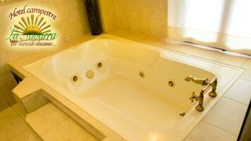 Una bañera grande y rectangular con múltiples grifos y un cabezal de ducha, un conjunto de escalones que llevan a ella, y un logotipo en la esquina superior izquierda.