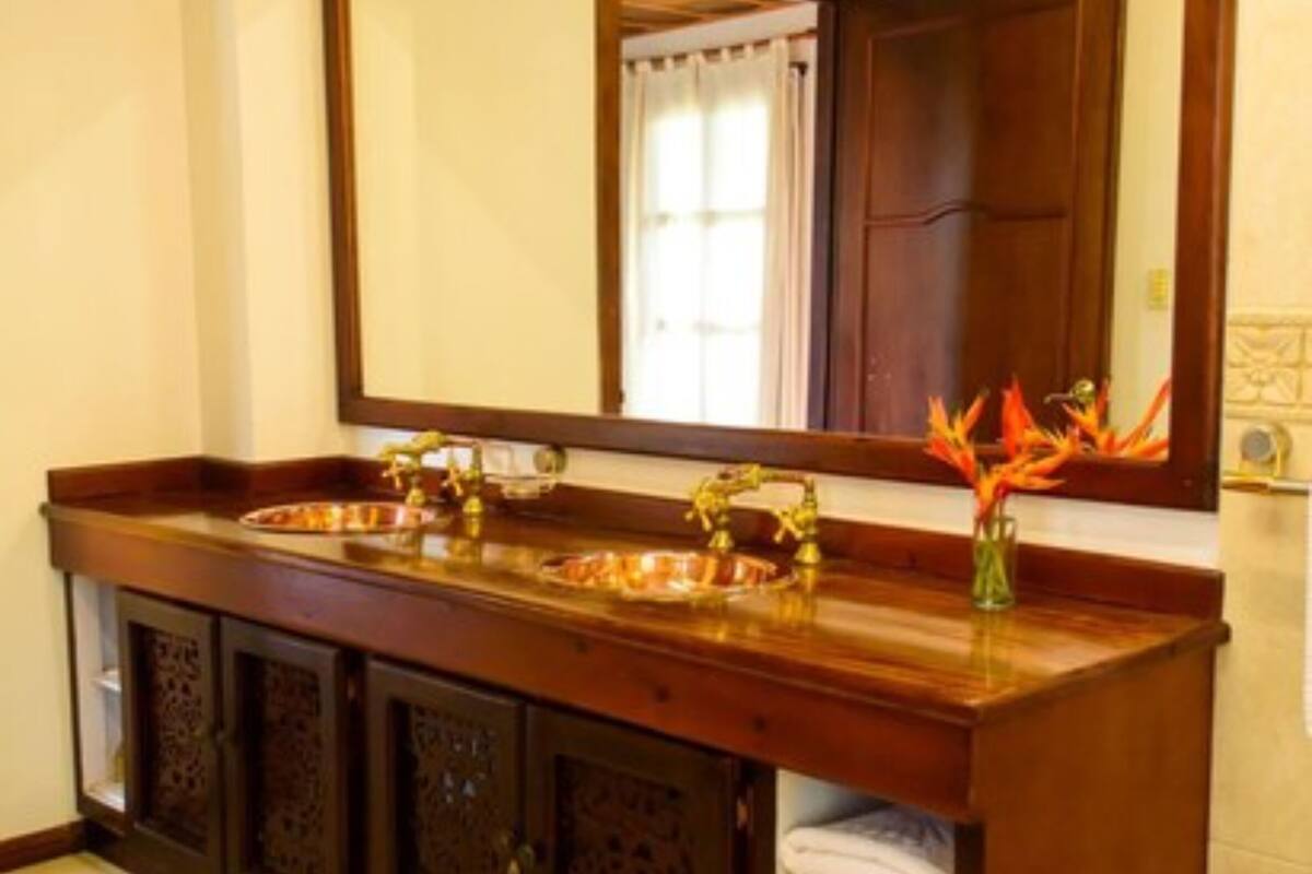 Un baño con tocador de madera, dos lavamanos, un espejo grande y un perchero para toallas.