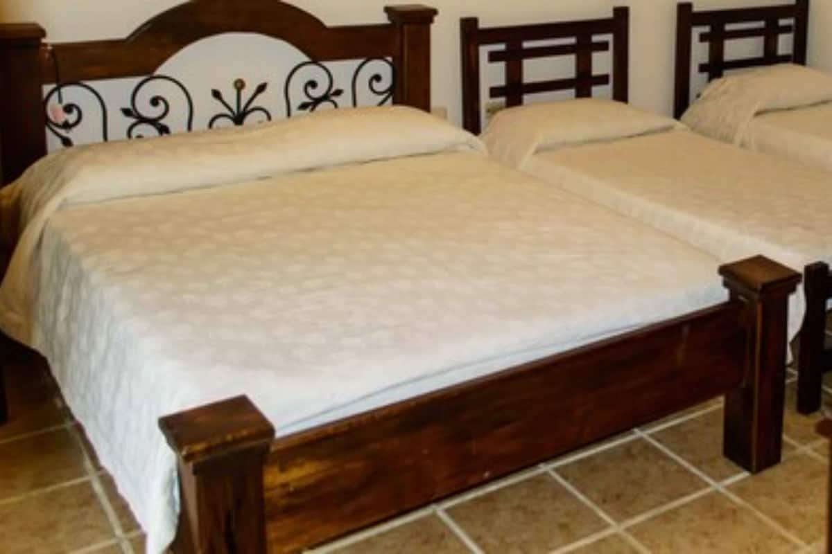 Una cama doble con estructura y cabecera de madera, dos almohadas y una mesita de noche con lámpara.