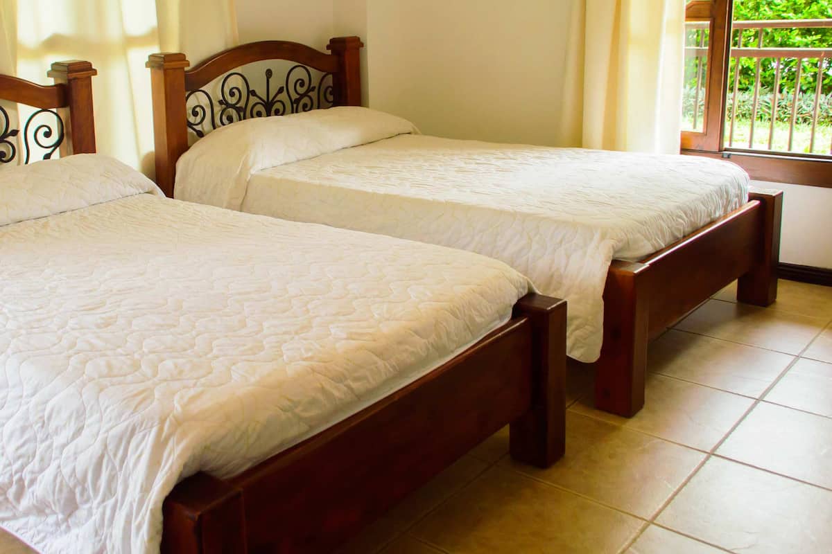Dos camas de madera con cabeceros metálicos en una habitación con piso de baldosas.