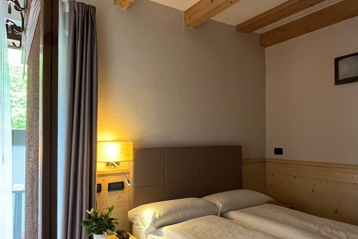 A hotel room with a bed, a nightstand, a lamp, a window with curtains, and a red carpet.