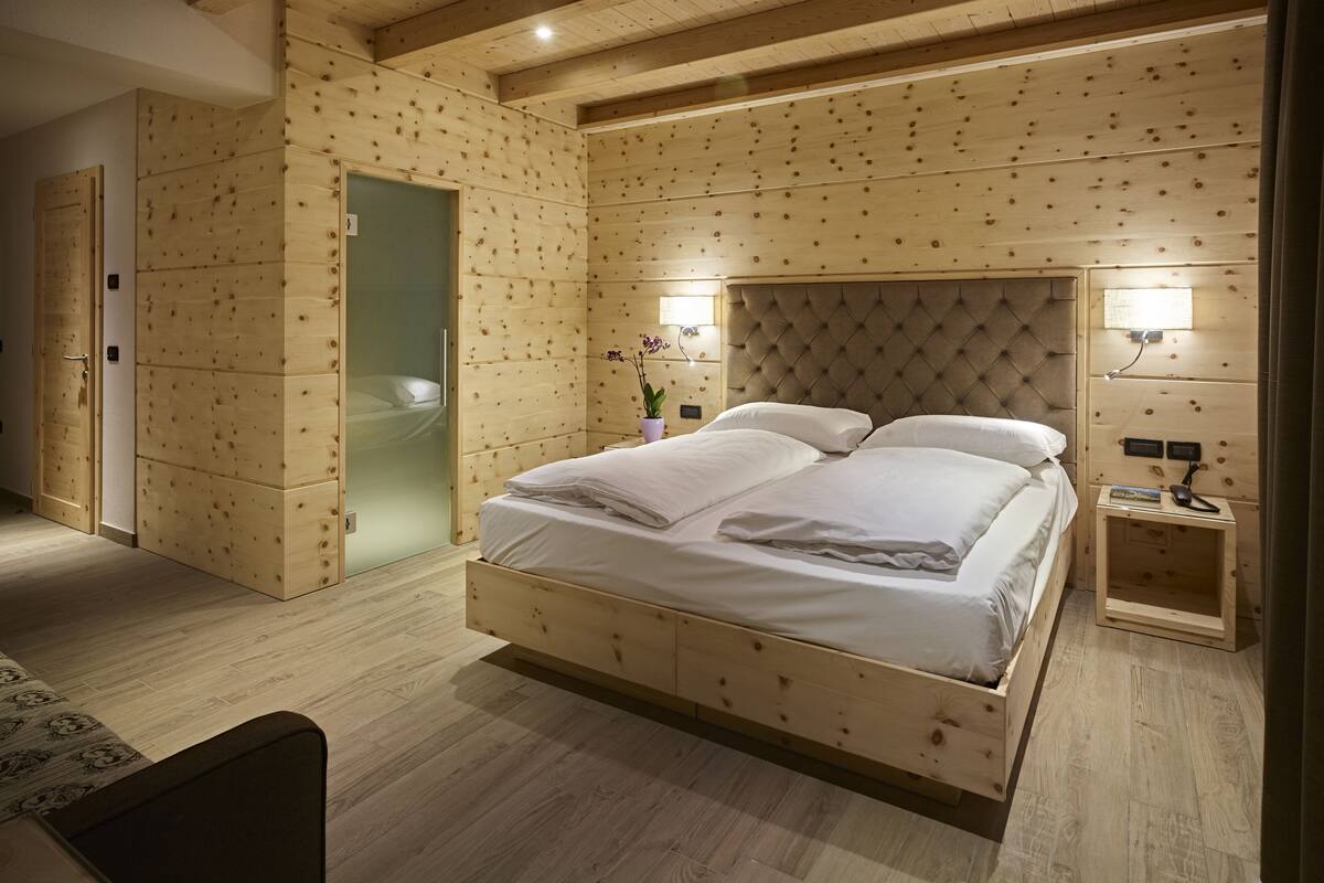 A wooden bedroom with a large bed, a nightstand, and a glass shower door.