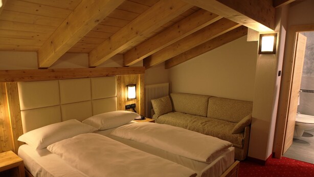 Una habitación con dos camas, vigas de madera, alfombra roja y un ventanal pequeño.