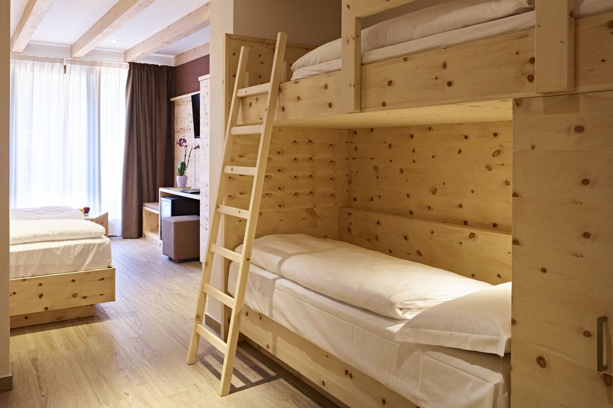 A room with bunk beds, a wooden ladder, a desk, and a window with curtains.