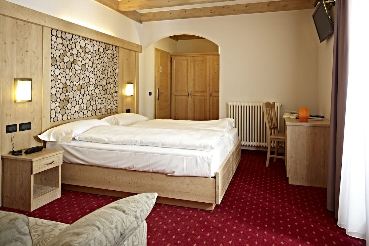 A hotel room with a wooden bed, a red carpet, a wooden desk, and a wall-mounted TV.