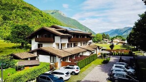 Un immeuble à plusieurs étages, de style architectural traditionnel, un parking avec plusieurs voitures et un paysage montagneux en arrière-plan.