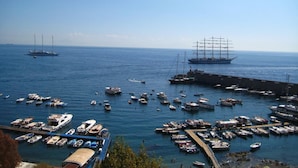 Un port de plaisance où sont amarrés différents types de bateaux, un grand navire et, au loin, un voilier à gréement complexe.